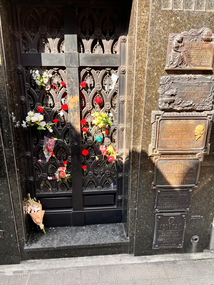 Fresh flowers tucked into the Duarte tomb’s black iron door beside bronze plaques honouring Evita