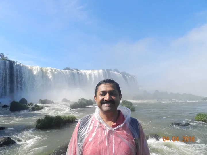 A visitor in a clear plastic poncho smiles before the wide curving wall of Iguazu Falls