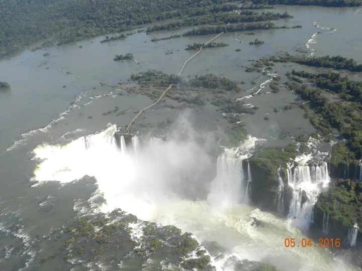 Aerial view of Iguazu Falls, spray rising from the horseshoe, a walkway crossing the river above