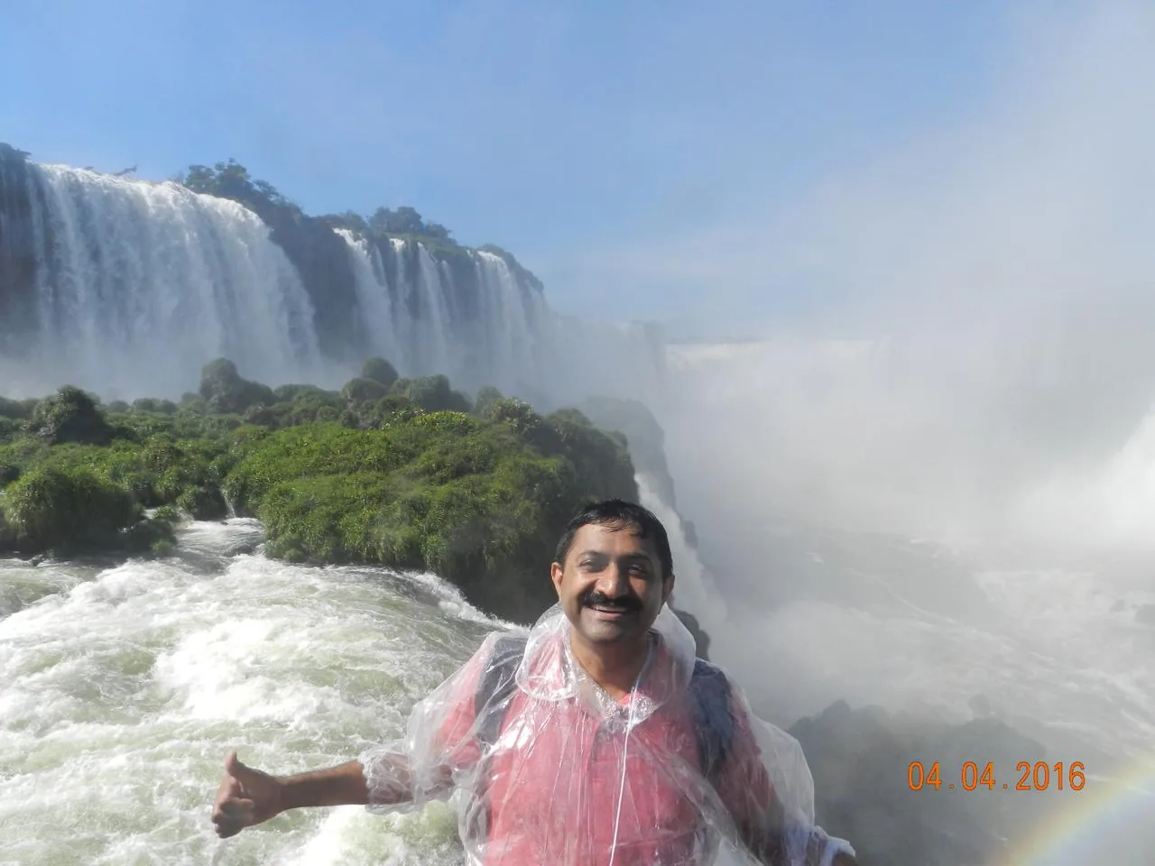 A poncho-clad visitor beside rushing water, cascades and moss-covered rocks behind at Iguazu