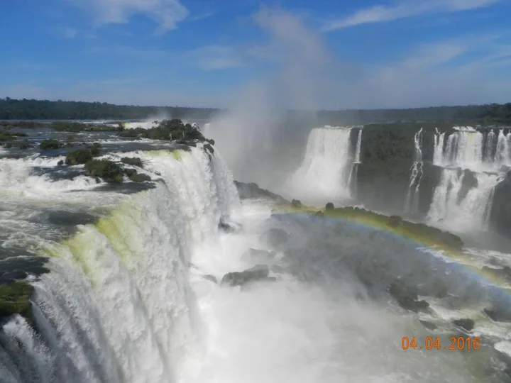 A rainbow arcs through the spray where multiple cascades of Iguazu Falls drop into the gorge