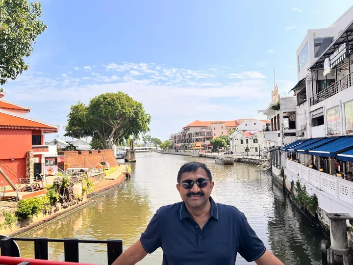 The Melaka River at midday, shophouses and blue riverside awnings lining both banks