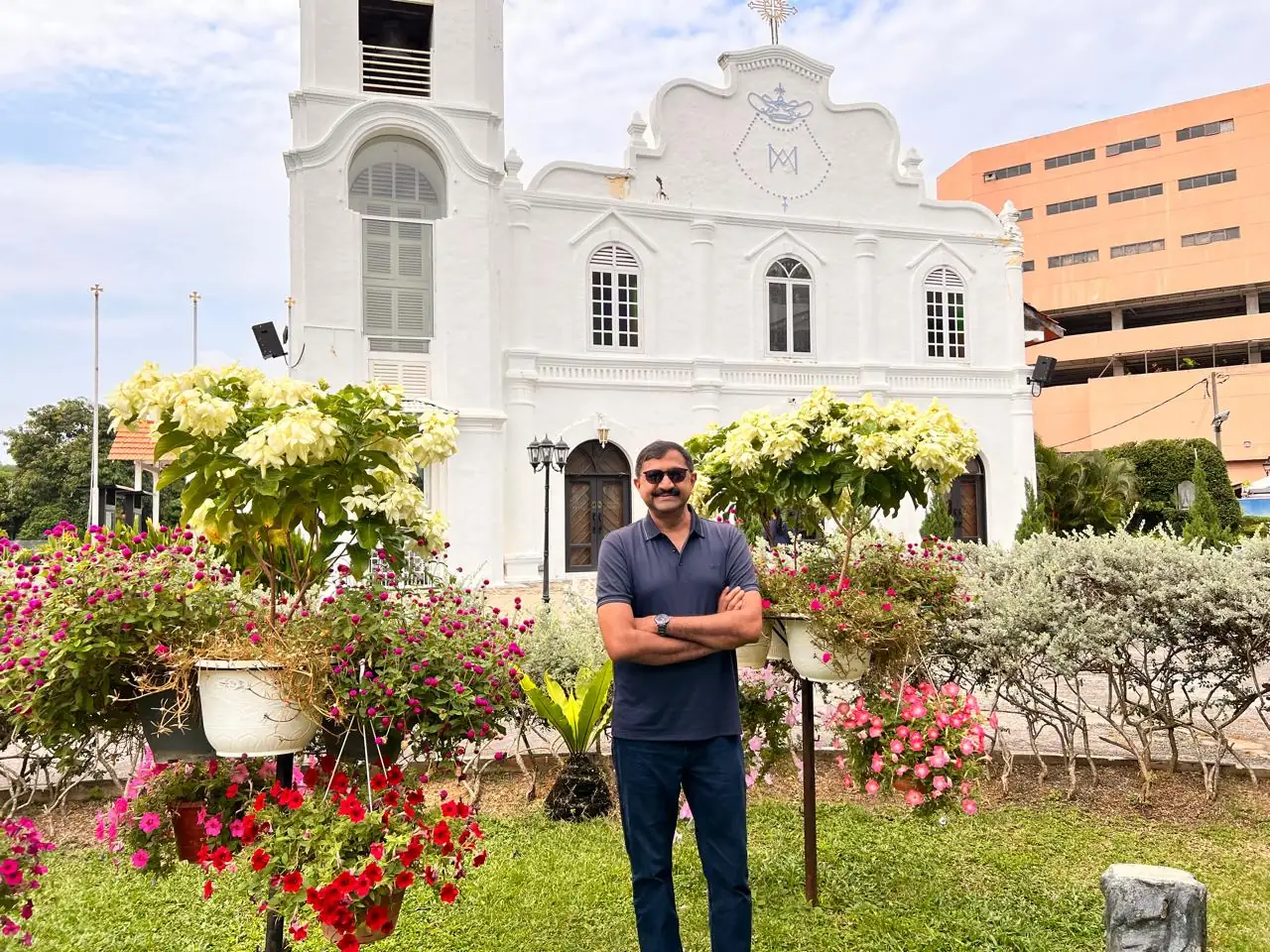 Whitewashed colonial church facade in Melaka behind hanging baskets of pink and red flowers