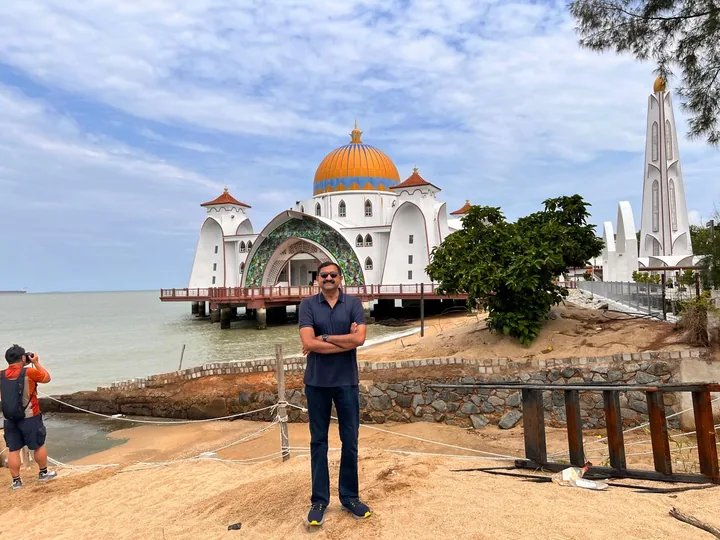 Melaka Straits Mosque on stilts over the water, gold dome against cloud, sandy shore in foreground